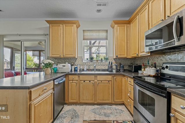 kitchen with a peninsula, a sink, visible vents, appliances with stainless steel finishes, and dark countertops