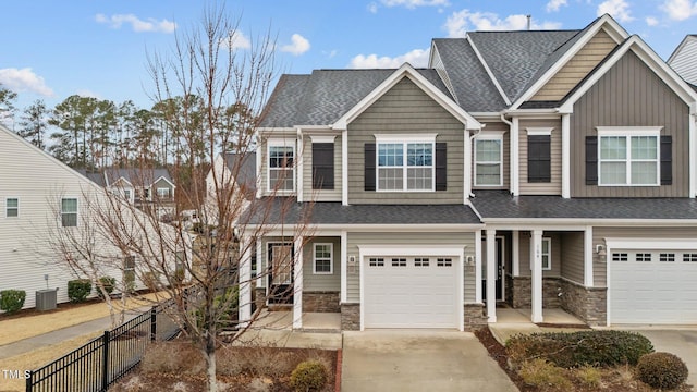 view of front of home with stone siding, a shingled roof, fence, and concrete driveway