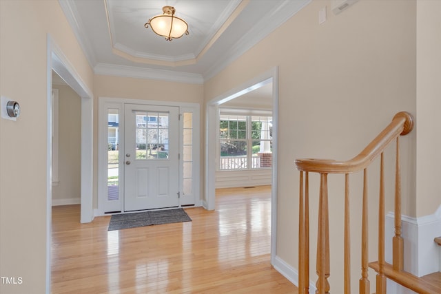 entryway with a tray ceiling, light wood-style flooring, baseboards, and ornamental molding