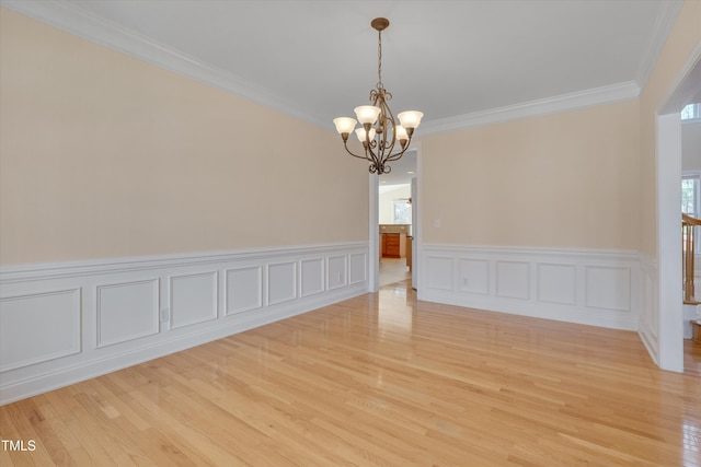 unfurnished room featuring an inviting chandelier, crown molding, and light wood-type flooring