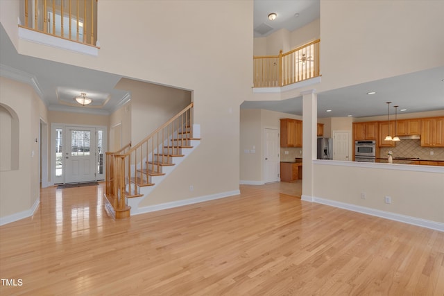 unfurnished living room featuring baseboards, stairs, light wood-style floors, a towering ceiling, and crown molding