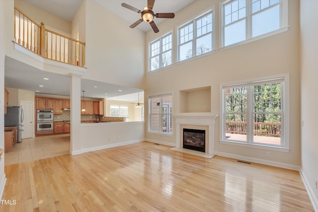 unfurnished living room featuring visible vents, a fireplace with flush hearth, light wood finished floors, baseboards, and ceiling fan