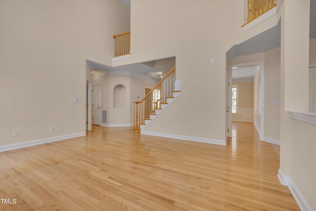 interior space featuring a towering ceiling, arched walkways, light wood-style flooring, and stairs