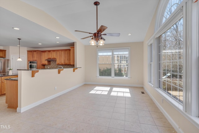 kitchen with ceiling fan, vaulted ceiling, stainless steel oven, decorative backsplash, and a kitchen breakfast bar