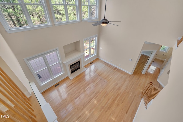 living area featuring a glass covered fireplace, a high ceiling, visible vents, and light wood-type flooring