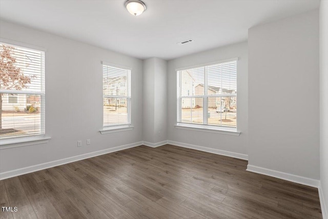 spare room featuring dark wood-type flooring, visible vents, and baseboards