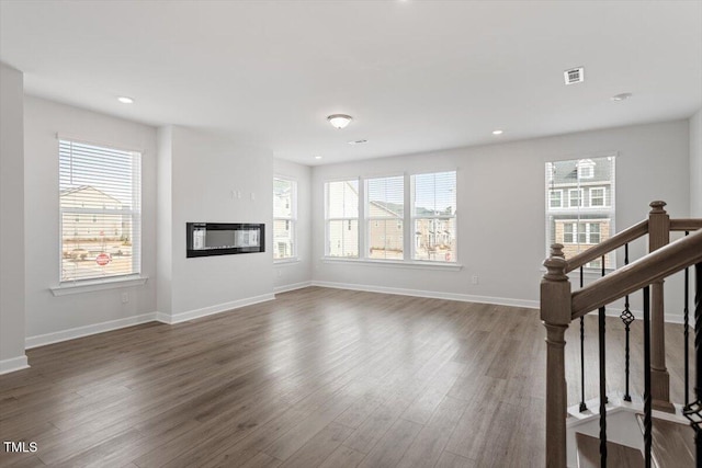 unfurnished living room with dark wood finished floors, recessed lighting, stairway, a glass covered fireplace, and baseboards