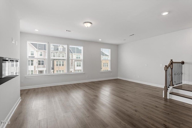 unfurnished living room featuring stairs, dark wood-type flooring, visible vents, and baseboards