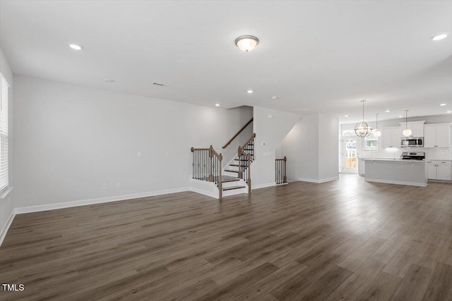 unfurnished living room featuring dark wood-style flooring, recessed lighting, stairway, an inviting chandelier, and baseboards