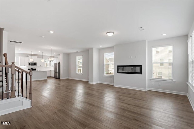 unfurnished living room with visible vents, a glass covered fireplace, dark wood-style floors, stairs, and recessed lighting