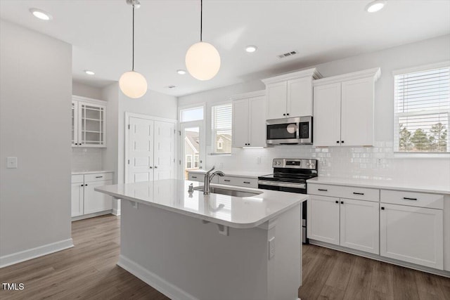 kitchen featuring a center island with sink, visible vents, appliances with stainless steel finishes, wood finished floors, and a sink