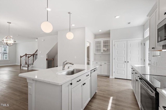 kitchen with pendant lighting, light wood finished floors, stainless steel appliances, decorative backsplash, and a sink