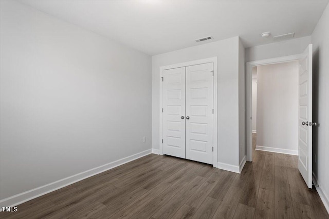 unfurnished bedroom featuring dark wood-style floors, a closet, visible vents, and baseboards