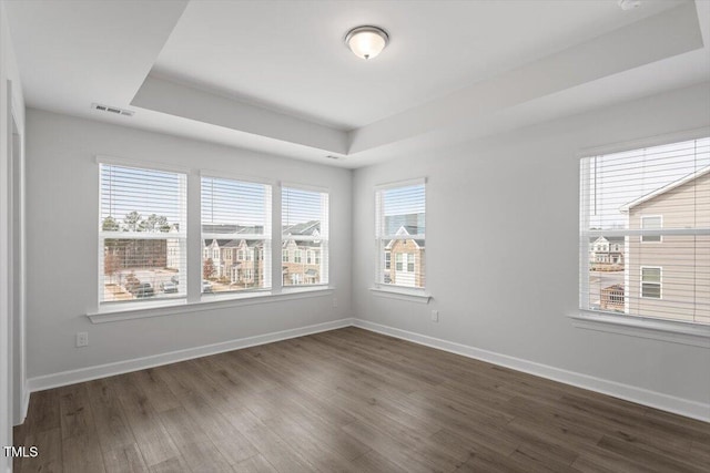 spare room featuring visible vents, baseboards, a raised ceiling, and dark wood-style flooring