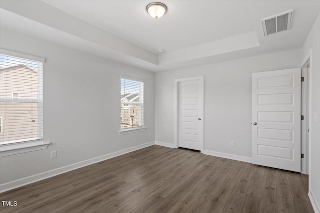 unfurnished bedroom with a raised ceiling, visible vents, dark wood finished floors, and baseboards