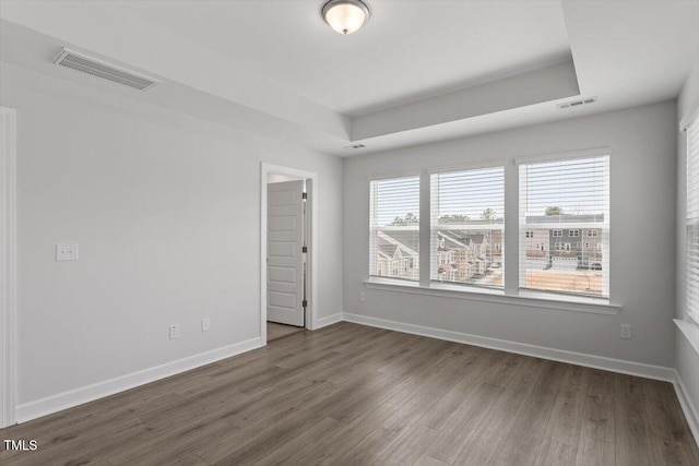 empty room with a tray ceiling, visible vents, baseboards, and wood finished floors