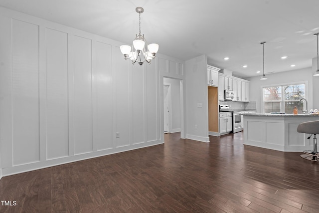 unfurnished living room featuring dark wood-style floors, recessed lighting, a decorative wall, and an inviting chandelier