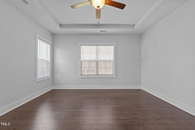 spare room with baseboards, a tray ceiling, dark wood-style flooring, and a healthy amount of sunlight