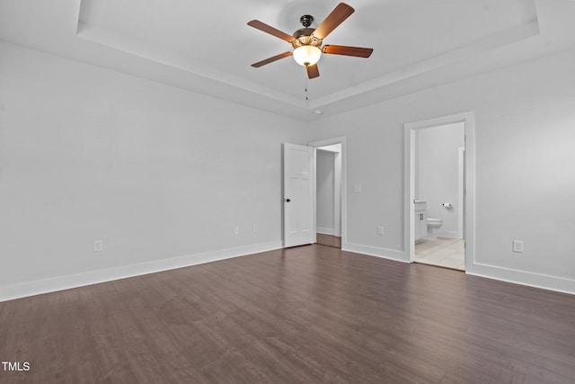 unfurnished bedroom featuring wood finished floors, a raised ceiling, connected bathroom, and baseboards