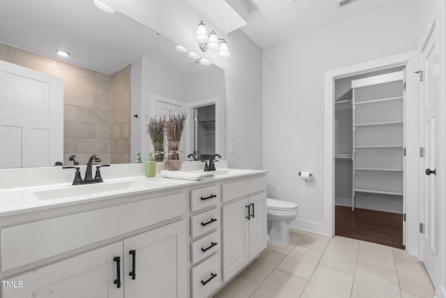 bathroom featuring a walk in closet, double vanity, a sink, and tile patterned floors