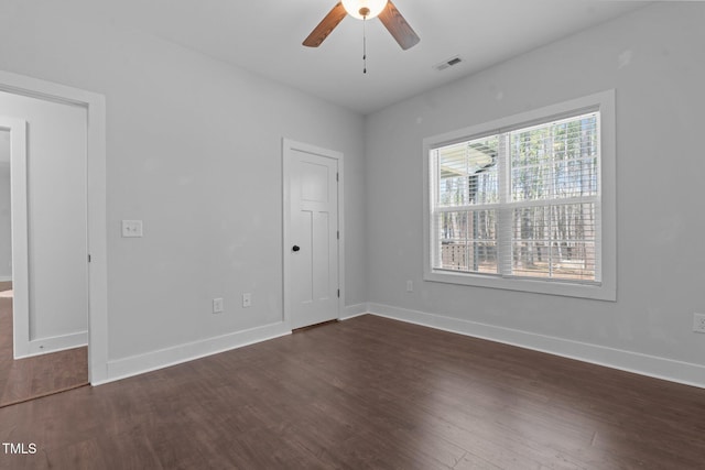 empty room featuring a ceiling fan, visible vents, dark wood finished floors, and baseboards