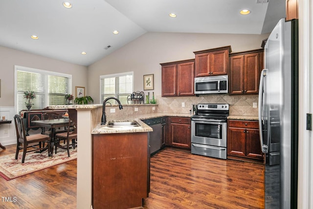 kitchen featuring dark wood-style floors, appliances with stainless steel finishes, vaulted ceiling, a sink, and a peninsula