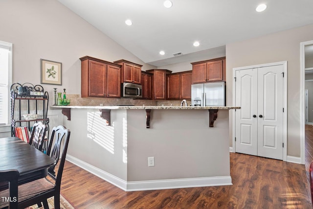 kitchen featuring stainless steel appliances, visible vents, a kitchen bar, and dark wood-style floors