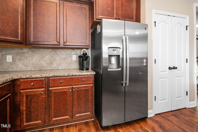 kitchen featuring stainless steel fridge, baseboards, dark wood finished floors, light stone counters, and backsplash