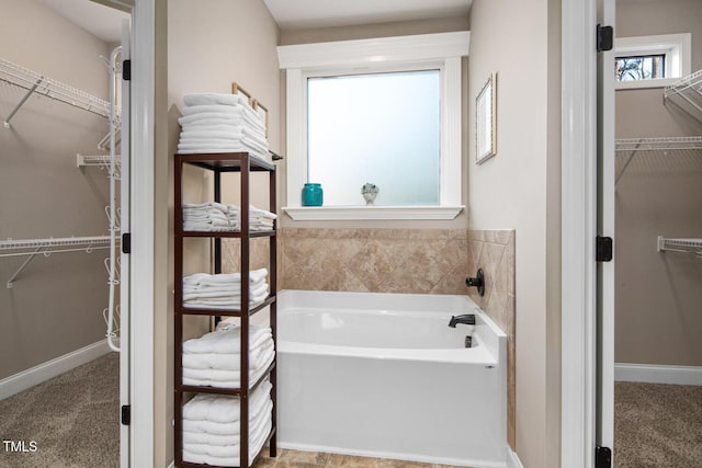 bathroom featuring a spacious closet, a bath, and baseboards