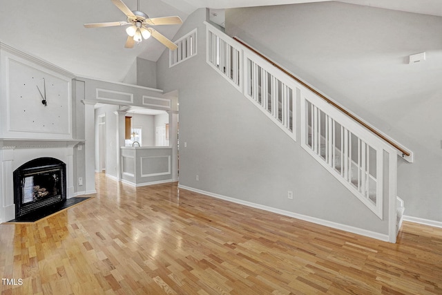 unfurnished living room featuring stairway, a ceiling fan, baseboards, light wood-style flooring, and a fireplace