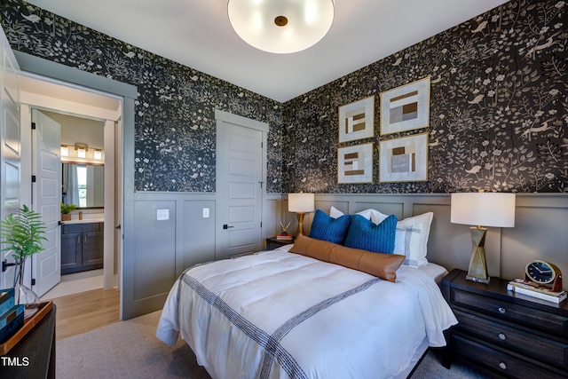 bedroom with wallpapered walls, a decorative wall, a wainscoted wall, and wood finished floors