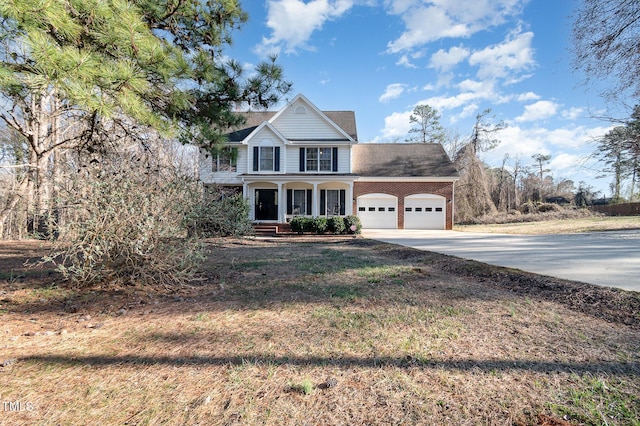 view of front of property with a garage, driveway, brick siding, and a porch