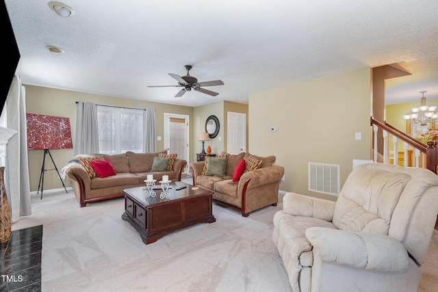 living room featuring a fireplace, light colored carpet, visible vents, a textured ceiling, and ceiling fan with notable chandelier