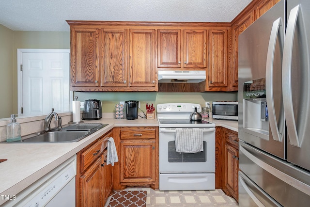 kitchen featuring white appliances, brown cabinetry, a sink, and under cabinet range hood