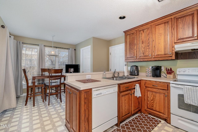 kitchen featuring under cabinet range hood, white appliances, a sink, light floors, and brown cabinetry