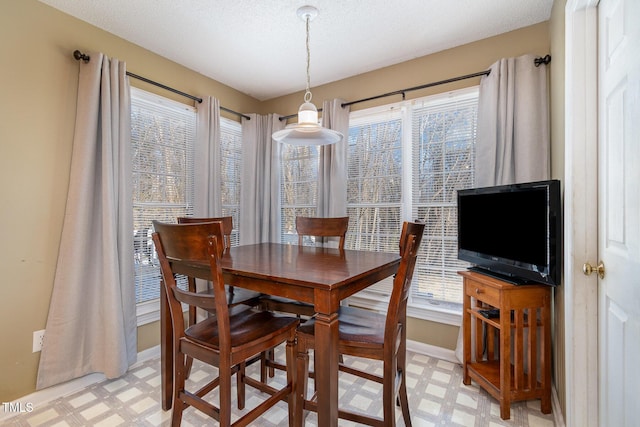 dining space with baseboards, a textured ceiling, and light floors