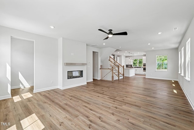 4706 Cypress Tree Ln, Raleigh, NC 27612 - unfurnished living room with stairs, light wood-style floors, a glass covered fireplace, recessed lighting, and baseboards