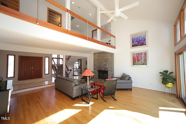 living room with a ceiling fan, a towering ceiling, stairway, wood finished floors, and a stone fireplace