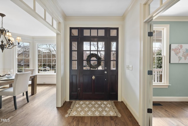 foyer featuring crown molding, a notable chandelier, wood finished floors, and baseboards