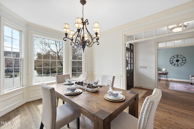 dining space featuring a chandelier, light wood-type flooring, ornamental molding, wainscoting, and a decorative wall