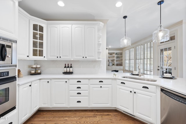 kitchen with glass insert cabinets, light wood-type flooring, hanging light fixtures, stainless steel appliances, and a sink