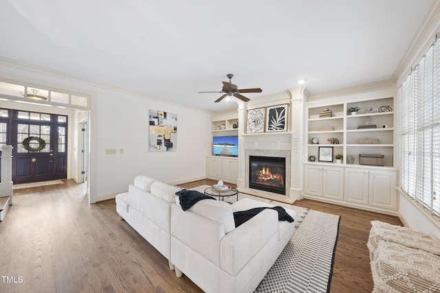 living area featuring baseboards, ornamental molding, wood finished floors, a glass covered fireplace, and a ceiling fan