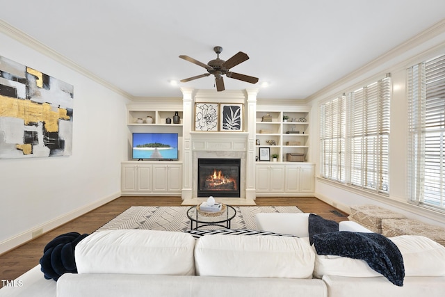 living area featuring crown molding, ceiling fan, baseboards, wood finished floors, and a glass covered fireplace