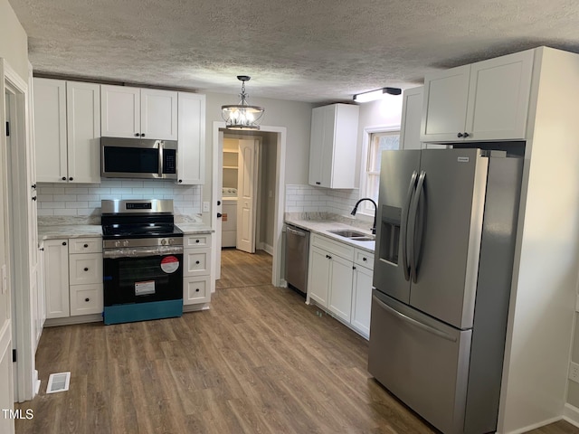 kitchen featuring visible vents, appliances with stainless steel finishes, white cabinets, a sink, and wood finished floors