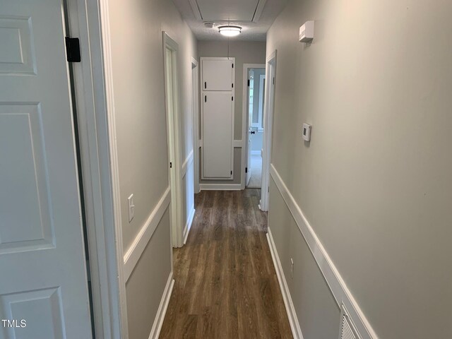 corridor featuring attic access, dark wood finished floors, and baseboards