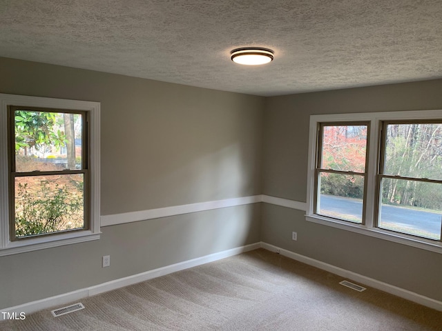 carpeted spare room with visible vents, a textured ceiling, and baseboards