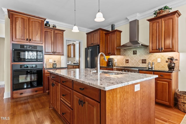 kitchen with a kitchen island with sink, ornamental molding, a sink, high end black refrigerator, and wall chimney range hood