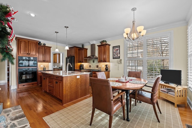 kitchen with light wood-type flooring, wall chimney exhaust hood, an inviting chandelier, and ornamental molding