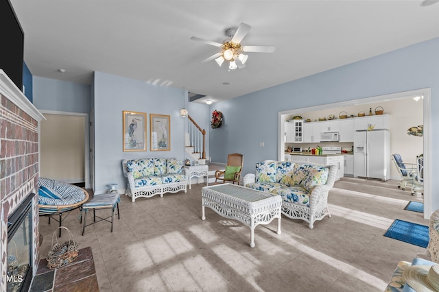 living room featuring a brick fireplace, stairway, and a ceiling fan