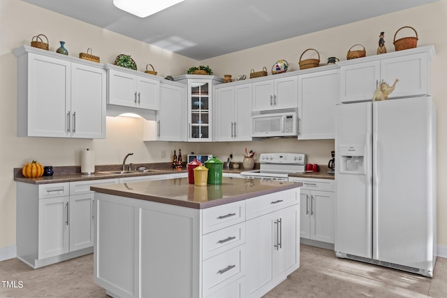 kitchen with white appliances, a sink, glass insert cabinets, white cabinetry, and a center island